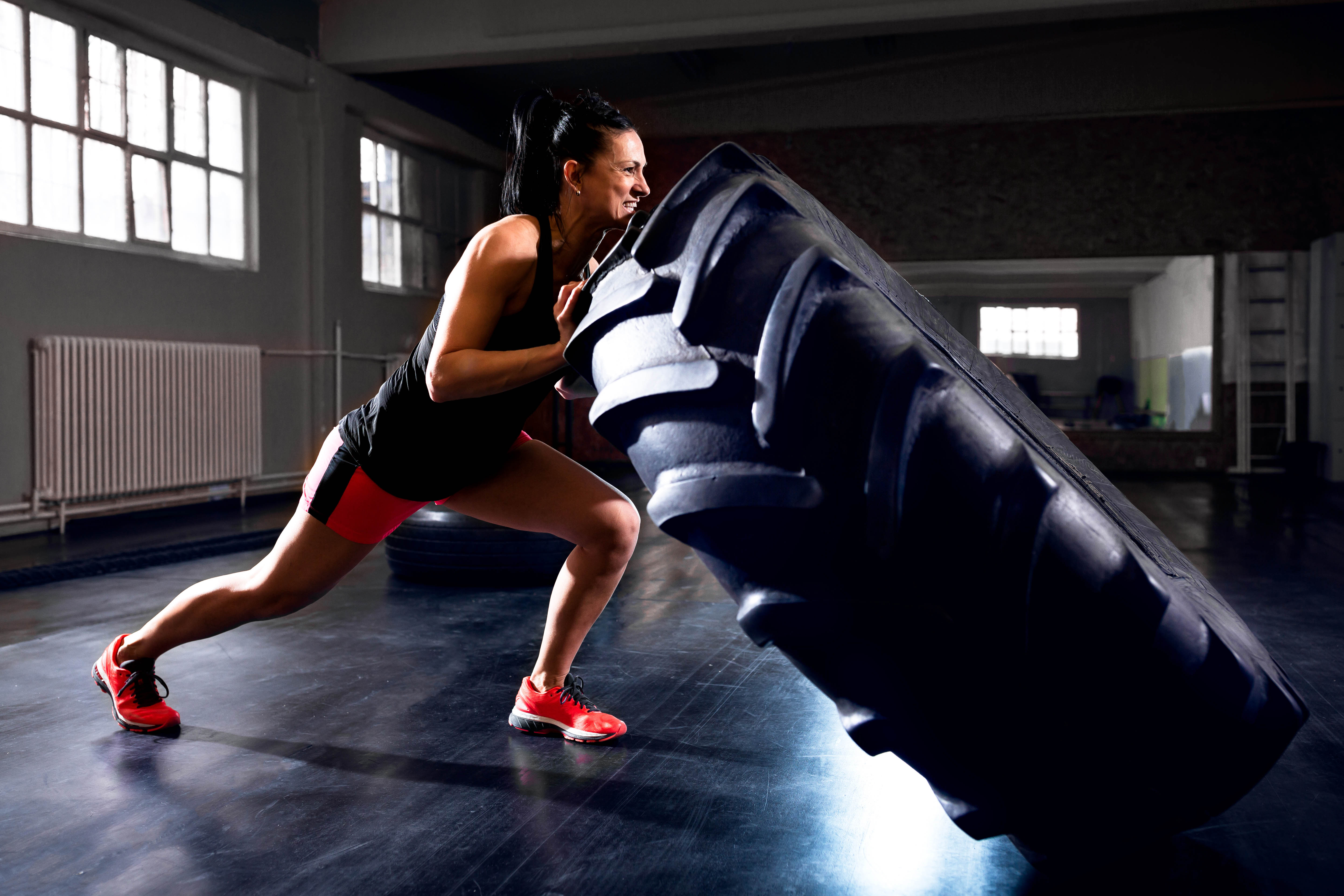 Younger woman flipping a tire in a gym setting Younger woman flipping a tire in a gym setting